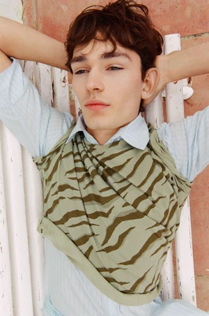 Model Noah Bates in a patterned green top and light blue shirt resting hands behind head