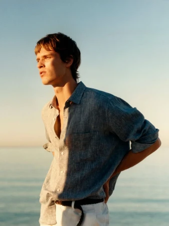 Model Yeray Allgayer wearing a blue linen shirt and white trousers against an ocean background for Massimo Dutti