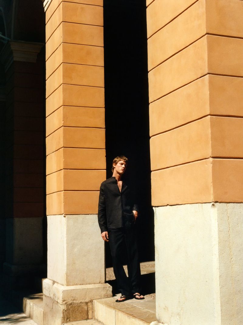 Man wearing a black shirt and trousers standing between large orange pillars for Massimo Dutti