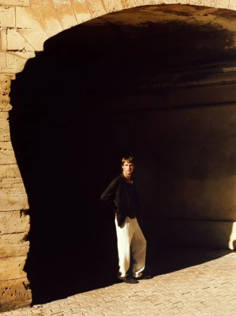 Model standing beneath a massive stone archway, wearing a dark jacket and pale trousers, shot by Jorge Perez Ortiz for Massimo Dutti.