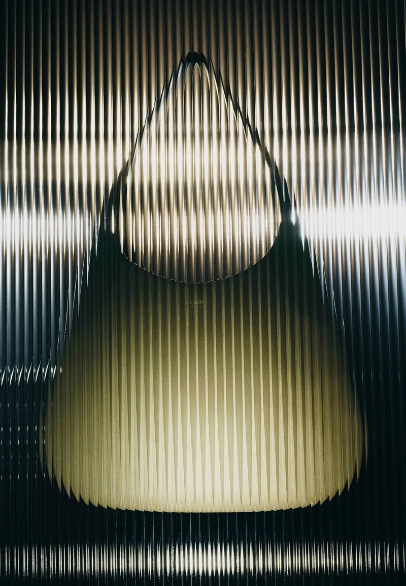 Black leather handbag positioned against a vertically fluted translucent glass background with warm lighting.