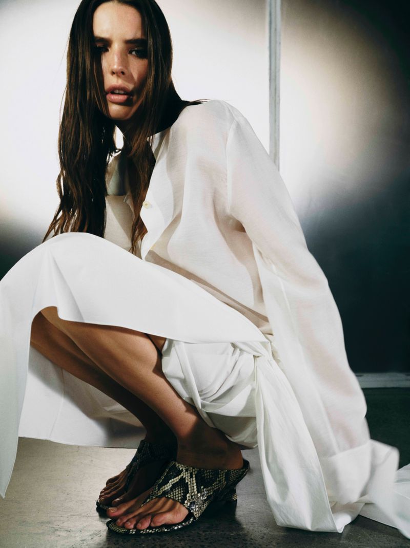 Model crouching wearing a long white shirt and snakeskin mules for Khaite S26 photographed by Hanna Tveite