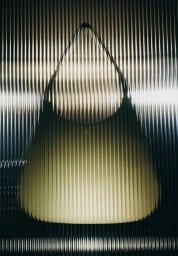 Black leather handbag positioned against a vertically fluted translucent glass background with warm lighting.