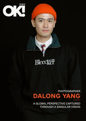 Man wearing a bright orange beanie and a black sweatshirt with white text against a solid dark background
