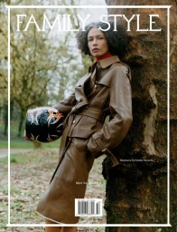 Model in brown leather coat leaning against a tree outdoors holding a helmet for Family Style magazine