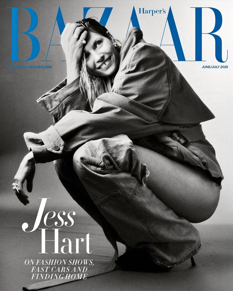 Jess Hart poses in a Harper's Bazaar magazine cover. Hart smiles, crouches and leans forward wearing a jacket and pants. Black and white.