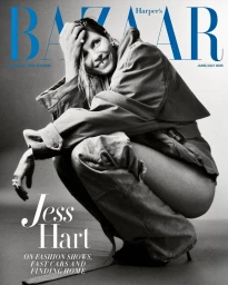 Monochrome magazine cover featuring a smiling woman crouching in an oversized jacket and jeans against a plain backdrop.
