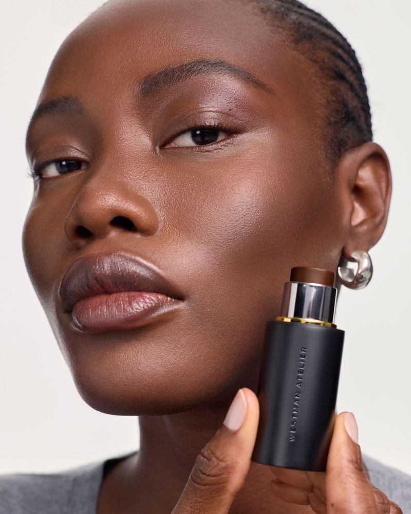 Close-up beauty portrait of a Black woman holding a Westman Atelier contour stick against a white background.