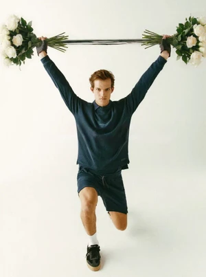 Model lifting a barbell loaded with large white rose bouquets on a white studio background for Trussardi.