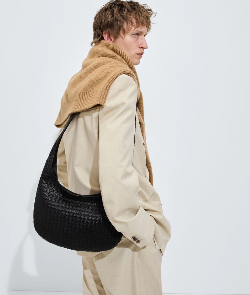 Model in cream blazer wearing a black woven leather shoulder bag against white