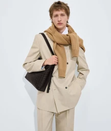 Model wearing a light beige suit and camel sweater with a dark woven leather shoulder bag against a white seamless background