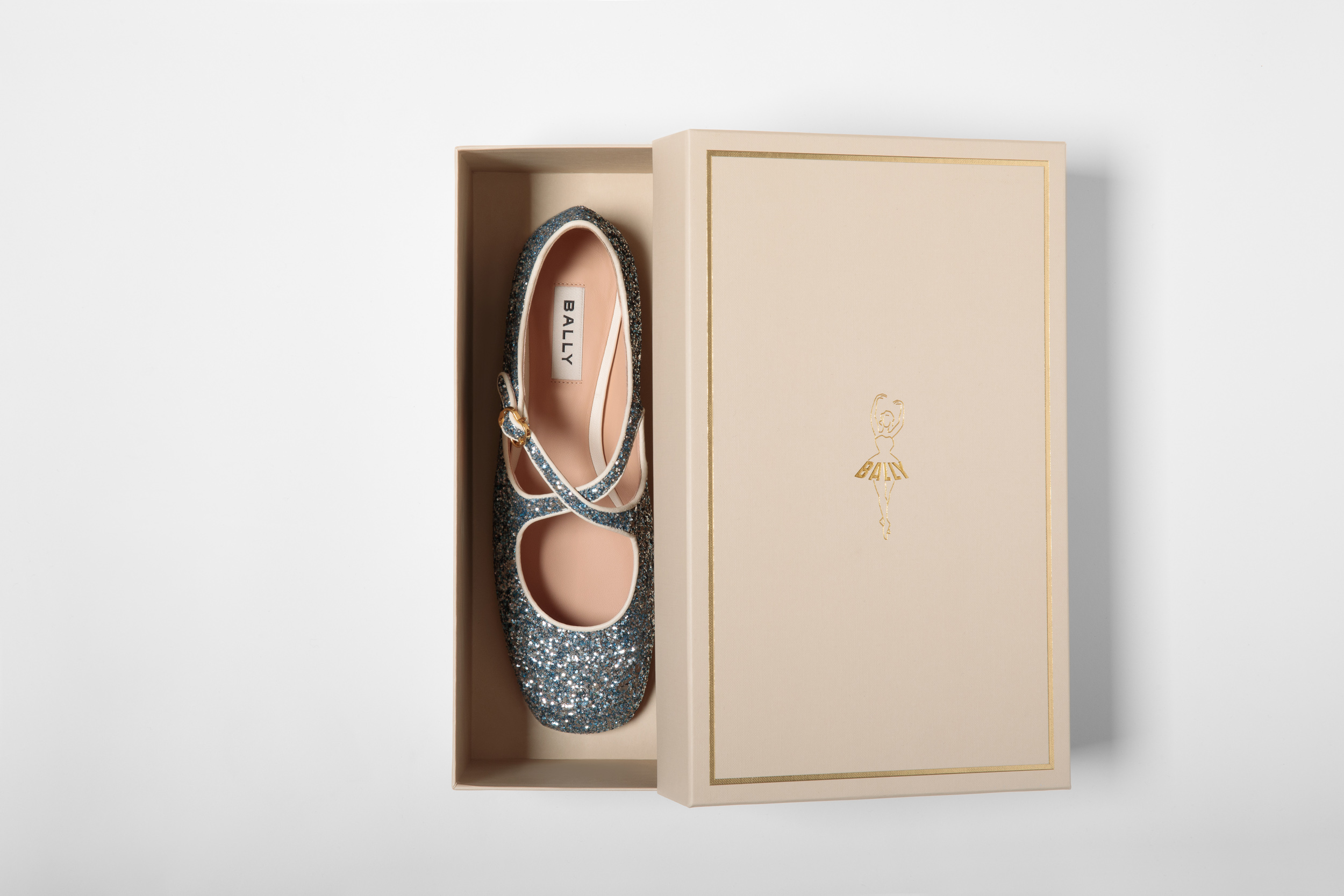 Glittery turquoise Bally flat shoe in a light peach-colored box with a gold logo on a white background, product photography.