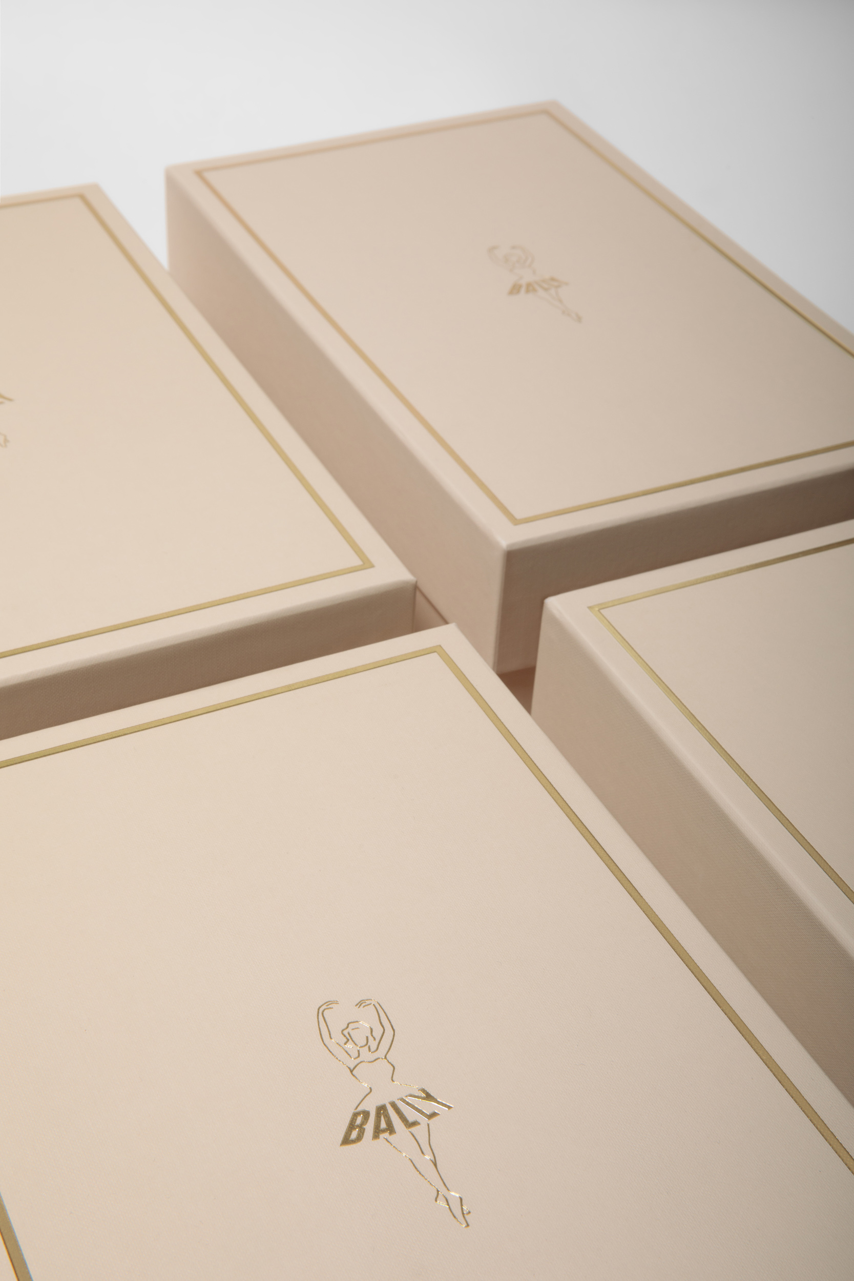 Four boxes with gold trim and a logo, arranged on a white surface, display luxury packaging for ballet or dance-related products.