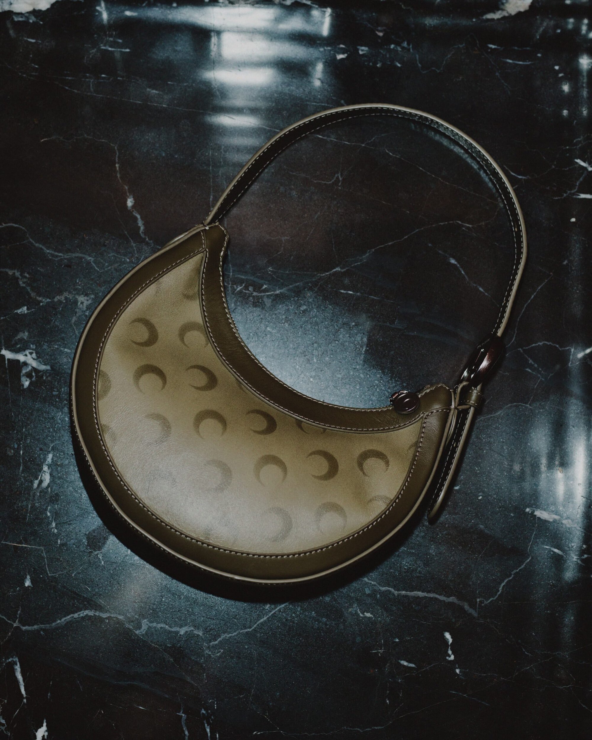 Marine Serre crescent moon patterned leather shoulder bag resting on a dark marble surface