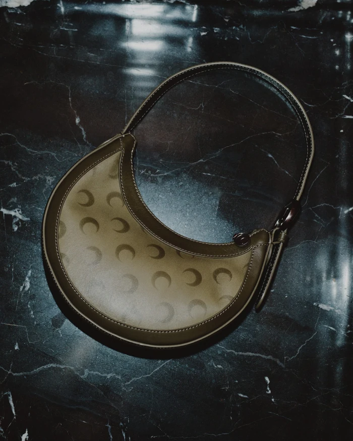 Marine Serre crescent moon patterned leather shoulder bag resting on a dark marble surface