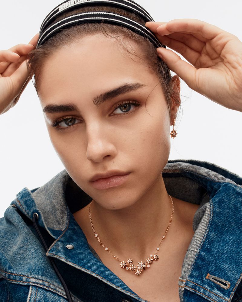 Close-up shot of a woman wearing a denim jacket and jewelry, including a necklace and earrings. She is also wearing a headband.