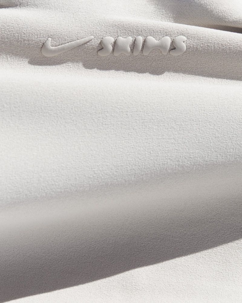 Close-up macro shot of off-white athletic fabric featuring a raised embossed Nike and SKIMS logo in neutral tones