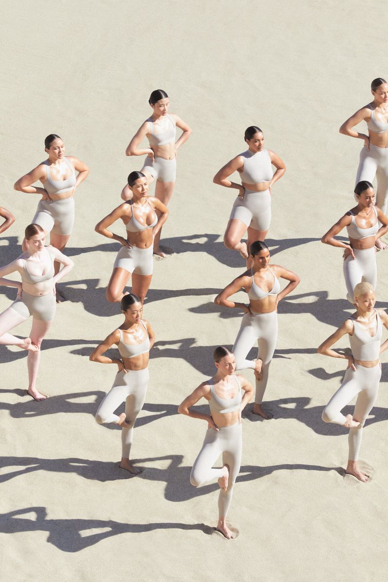 Group of female models in matching neutral activewear posing outdoors on sandy terrain under bright sunlight.