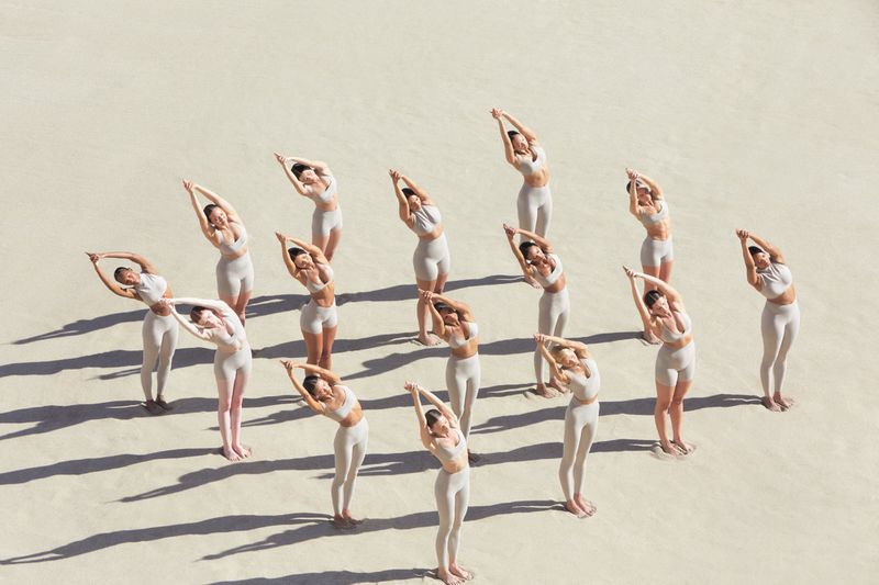 An aerial shot of a group of female models in neutral activewear posing on a sandy terrain.