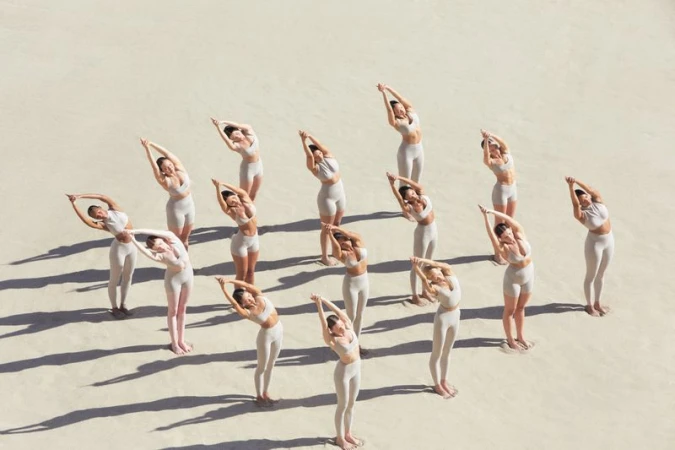 An aerial shot of a group of female models in neutral activewear posing on a sandy terrain.