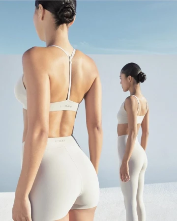 Two women wearing matching white athletic wear standing against a bright minimal outdoor background.