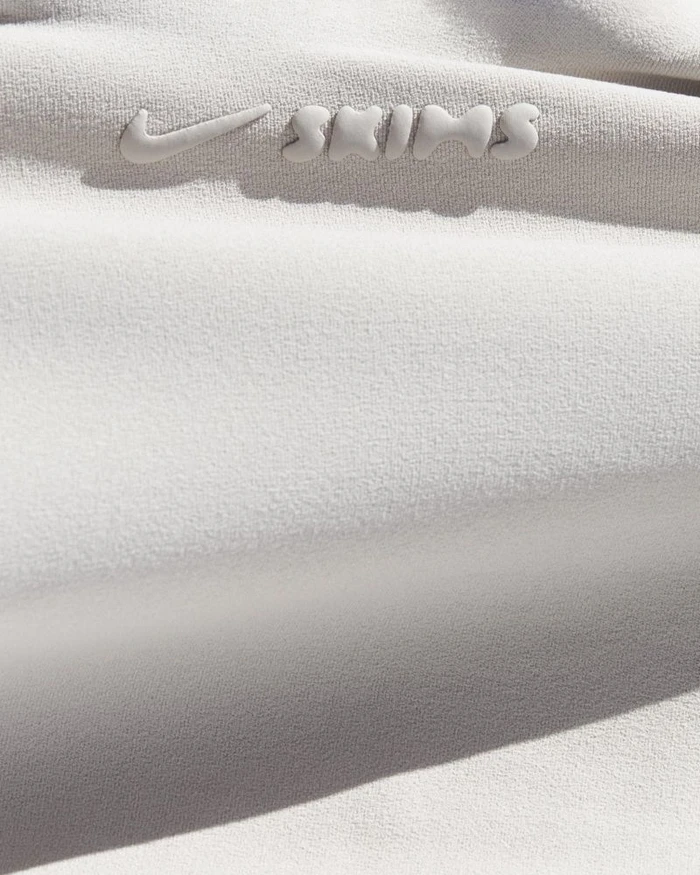 Close-up macro shot of off-white athletic fabric featuring a raised embossed Nike and SKIMS logo in neutral tones