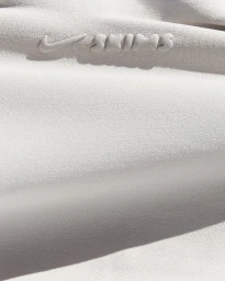 Close-up macro shot of off-white athletic fabric featuring a raised embossed Nike and SKIMS logo in neutral tones