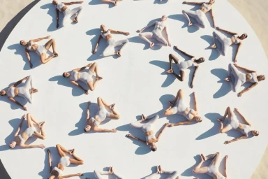An overhead view of multiple models lying in a circular formation on a white platform wearing matching activewear sets.