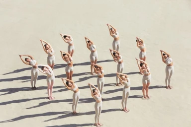 An aerial shot of a group of female models in neutral activewear posing on a sandy terrain.
