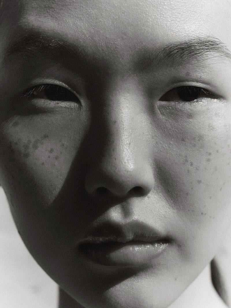 Close-up portrait of a young adult woman with fair skin and freckles, captured in black and white with natural, even lighting.