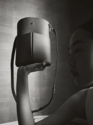 Model Peng Chang holds up a structured leather bucket bag in a black and white editorial photograph for RSVP Paris.