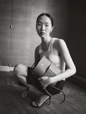 Model squatting on a wooden floor holding a structured leather handbag for RSVP Paris