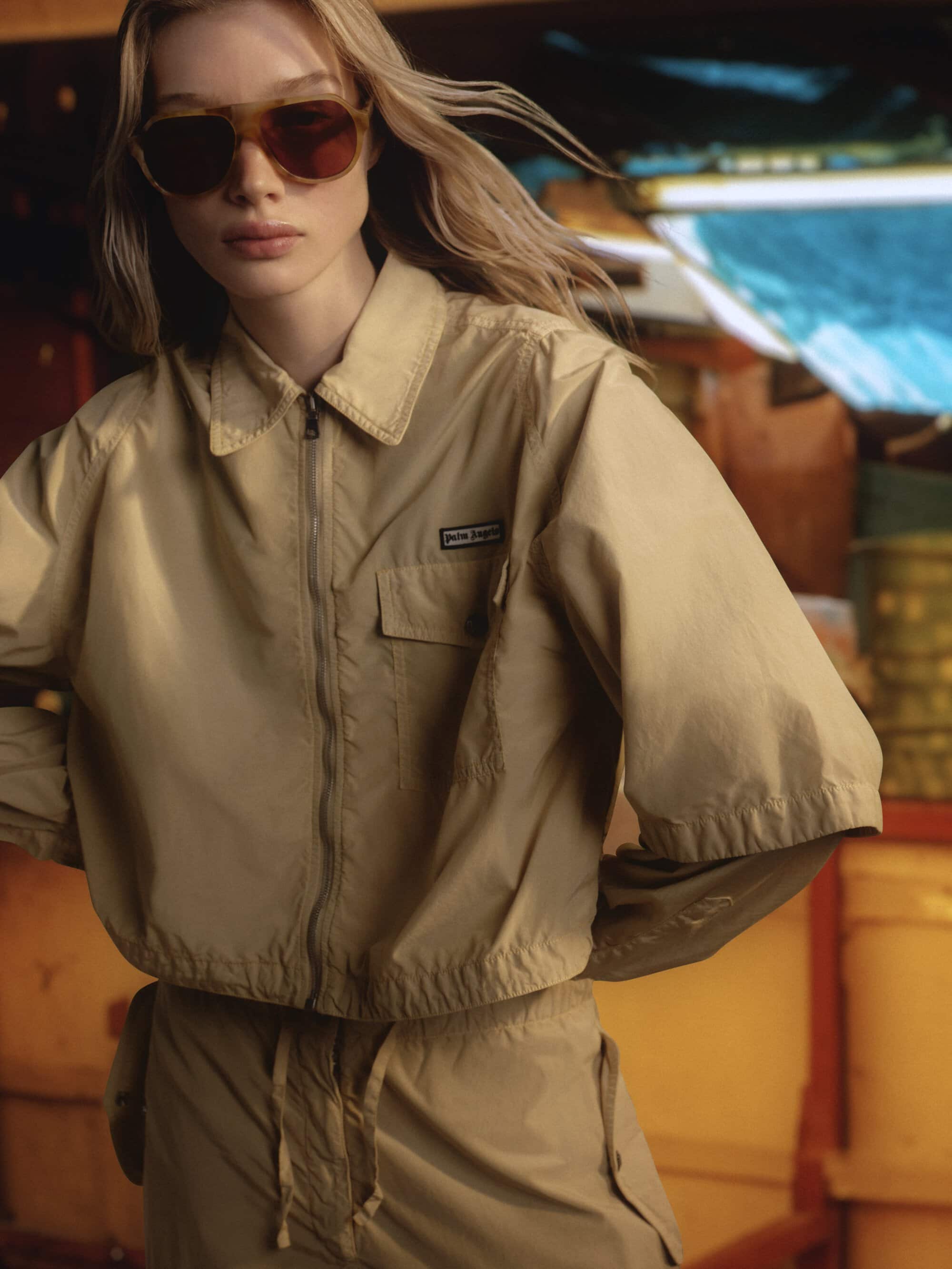 Model in oversized beige jacket and sunglasses posing in a boat interior for Palm Angels Island Speed campaign