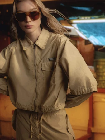 Model in oversized beige jacket and sunglasses posing in a boat interior for Palm Angels Island Speed campaign