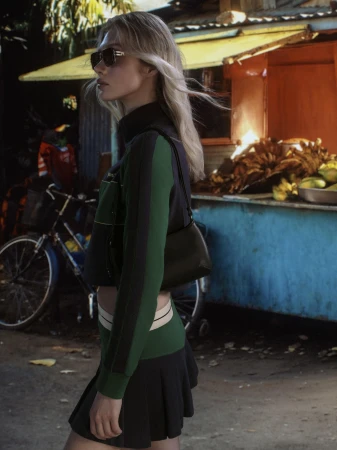 Blonde woman in dark sunglasses wearing a green and black athletic outfit standing outdoors near a street vendor stand