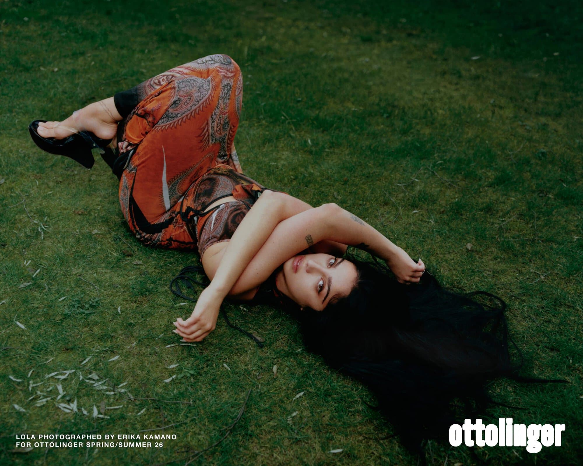 Model lying on grass wearing patterned orange clothing, photographed for Ottolinger Spring 2026 ad campaign