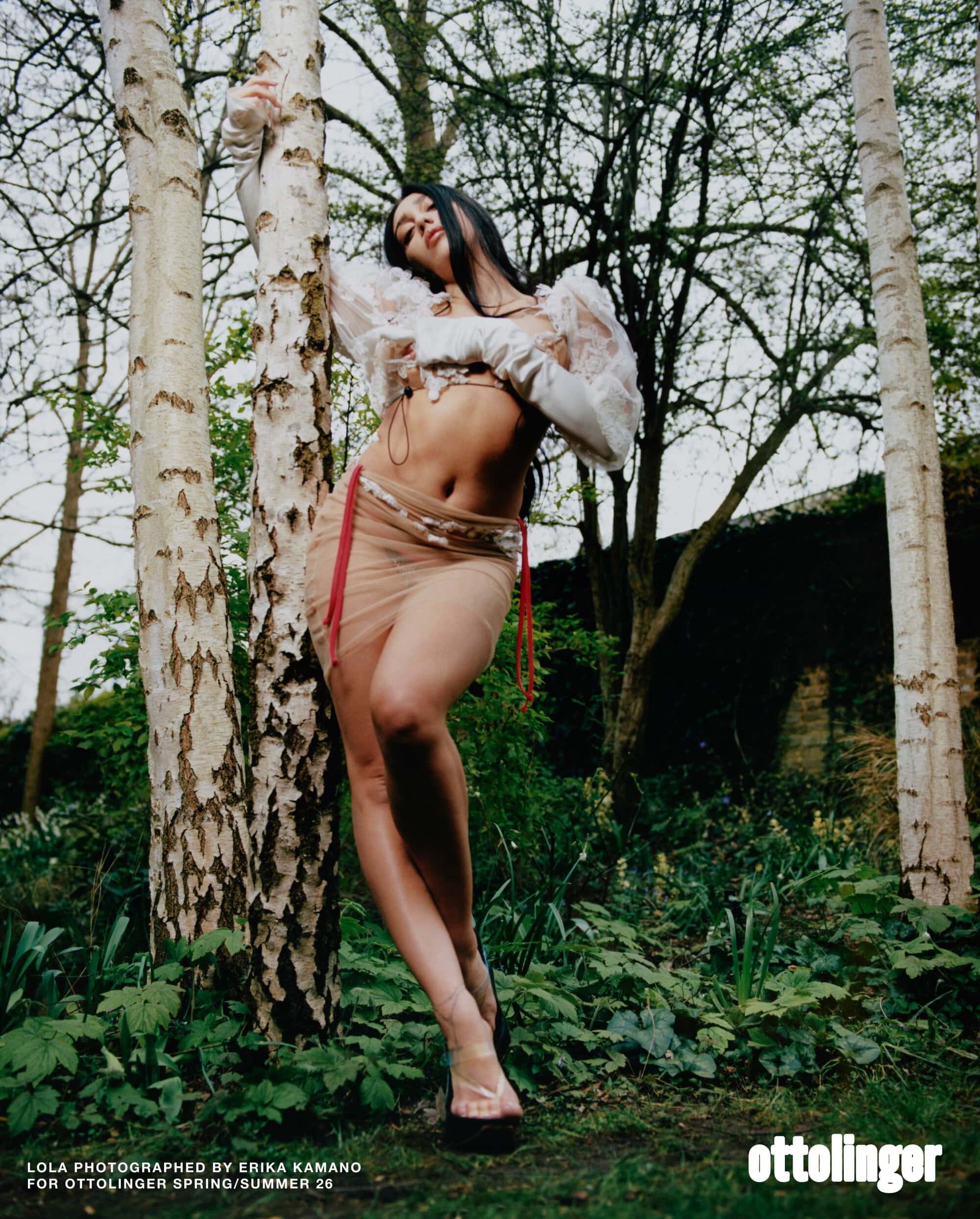 Model Lola Leon leaning against a birch tree in a woodland setting wearing sheer apparel for Ottolinger Spring 2026 ad campaign