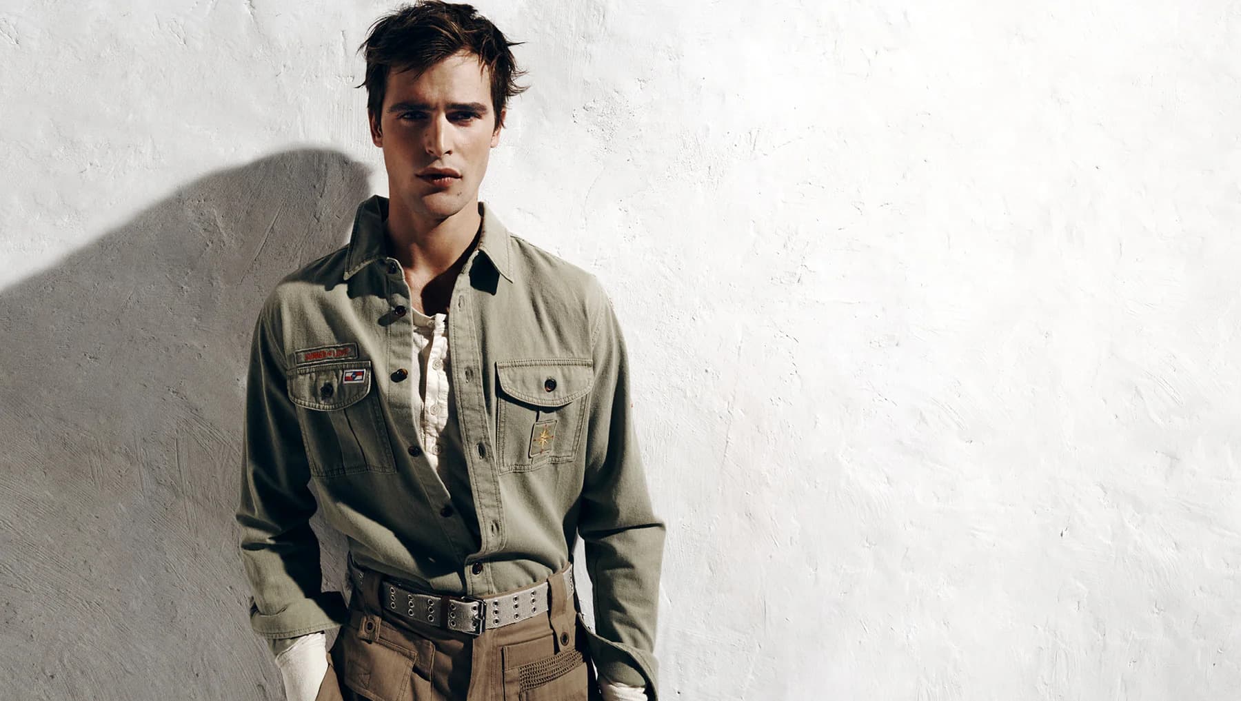Parker Van Noord wearing an olive green button-down shirt standing against a textured white wall for Isabel Marant.