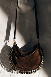 Brown suede shoulder bag with metallic embellishments hanging against a textured white wall.