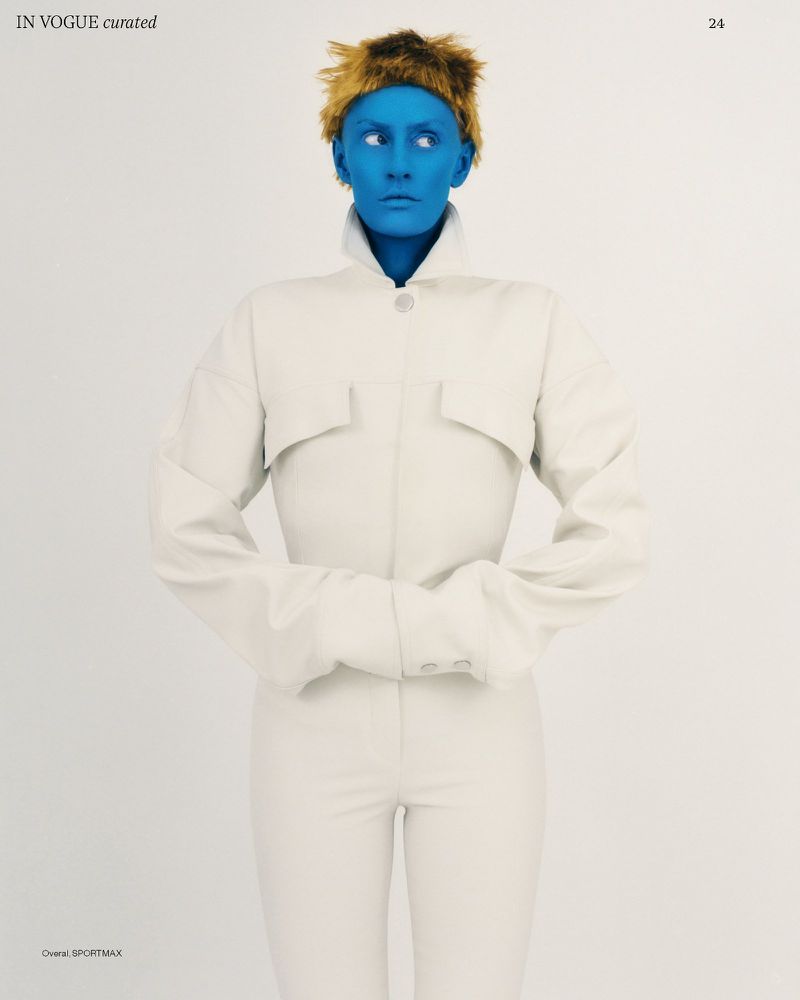 Person with blue skin and blonde hair in a white Sportmax jumpsuit, against a white backdrop in a studio fashion editorial.