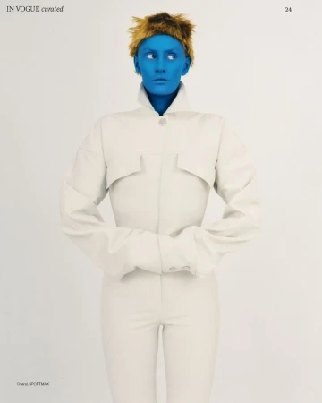Person with blue skin and blonde hair in a white Sportmax jumpsuit, against a white backdrop in a studio fashion editorial.