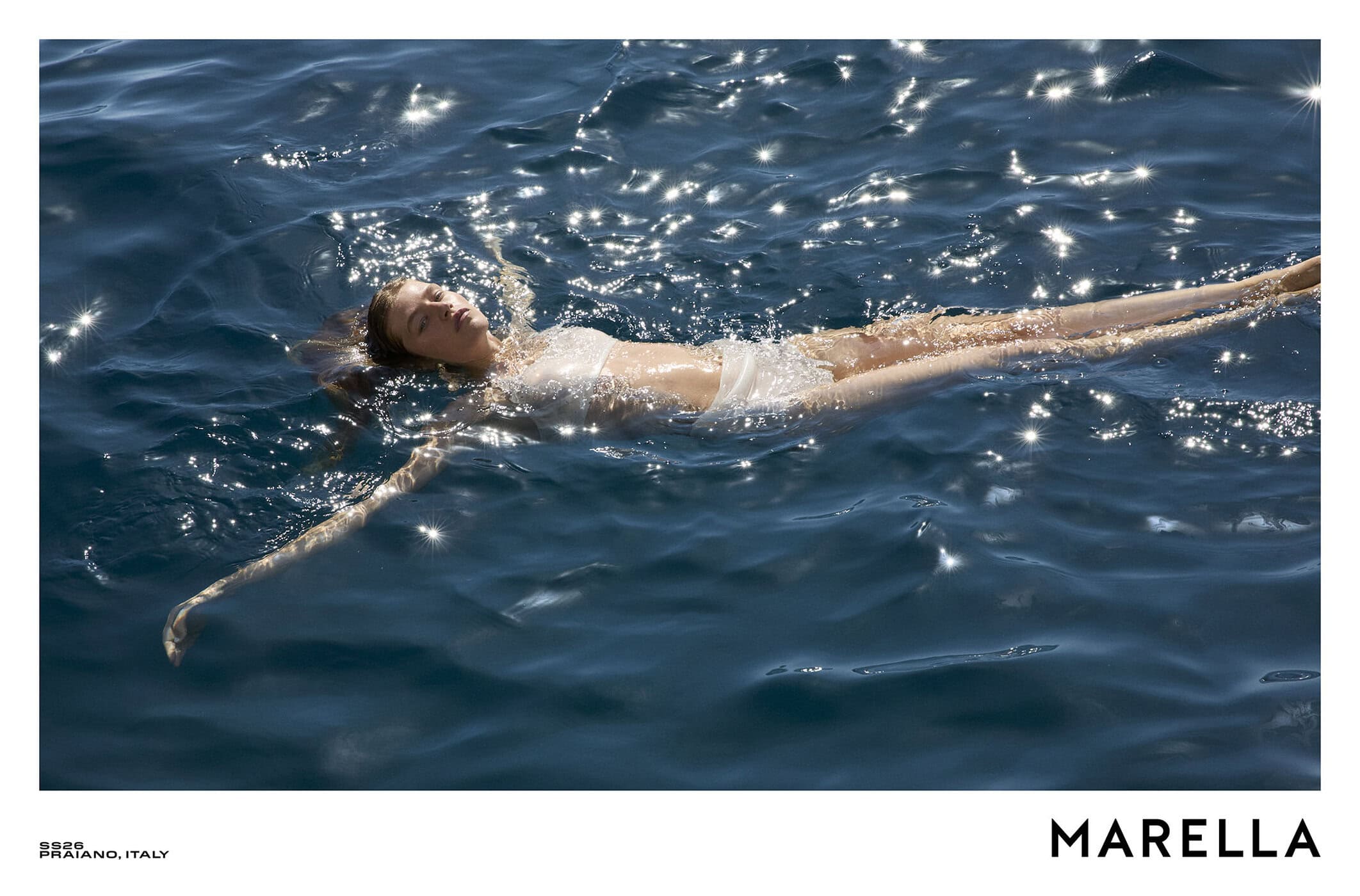 Model floating flat on her back in deep blue ocean water sparkling with bright sun glints
