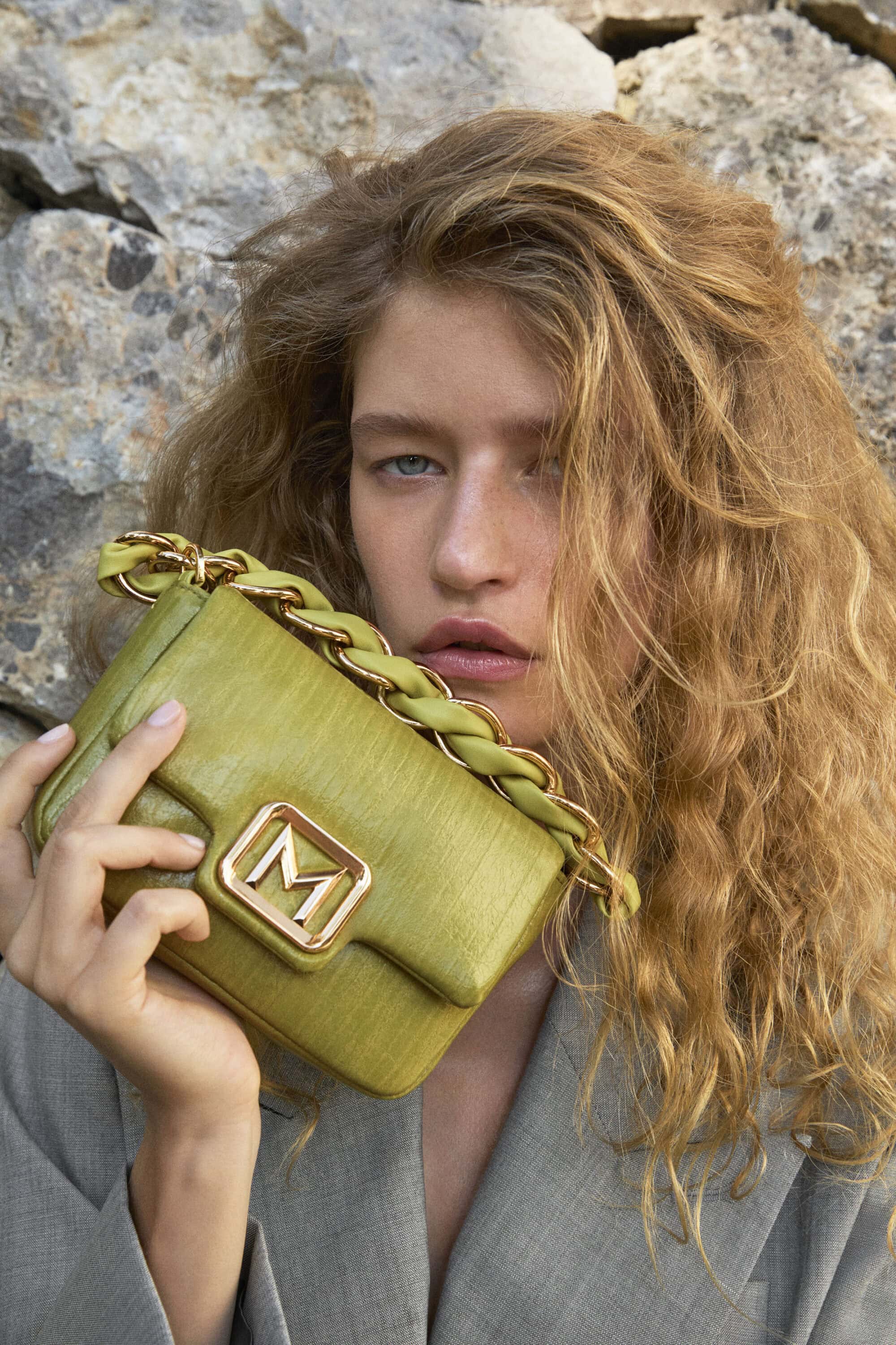 Model holding a green leather handbag against a rocky background for the Marella summer 2026 campaign.