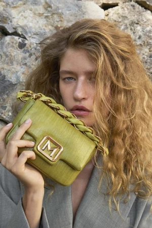 Model holding a green leather handbag against a rocky background for the Marella summer 2026 campaign.