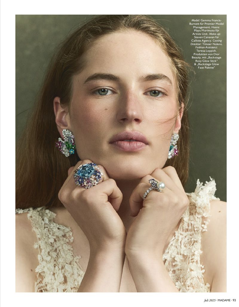 Close-up of a fashion model with large earrings and rings, posing in a photo studio with a green background and wearing a lace dress.