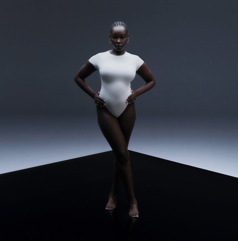 Model Ajok Daing wearing a white bodysuit against a dark studio background