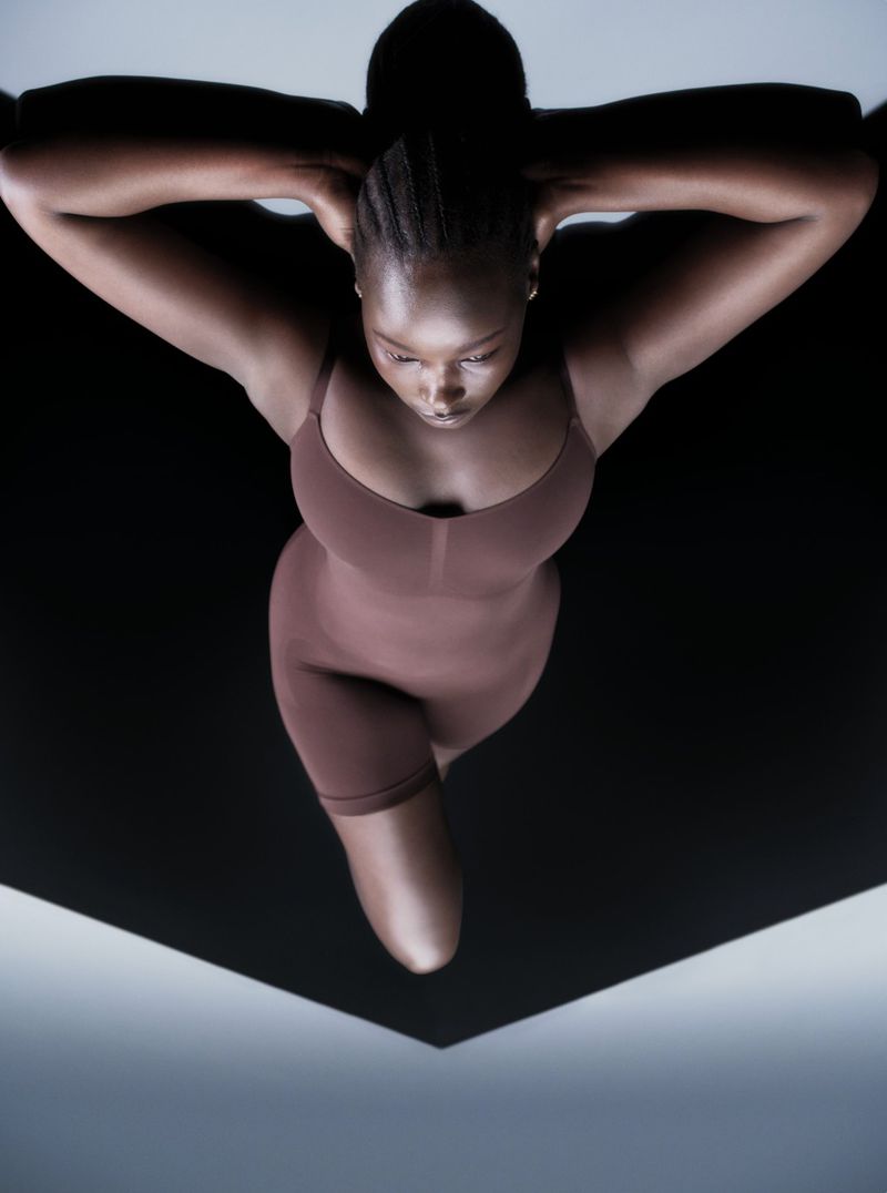Model Ajok Daing in a brown bodysuit photographed from overhead against a black and grey studio background