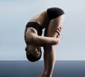 Model wearing black underwear bending forward in a studio against a light grey backdrop