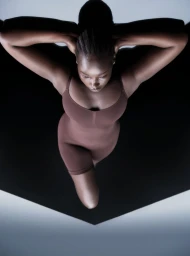 Model Ajok Daing in a brown bodysuit photographed from overhead against a black and grey studio background