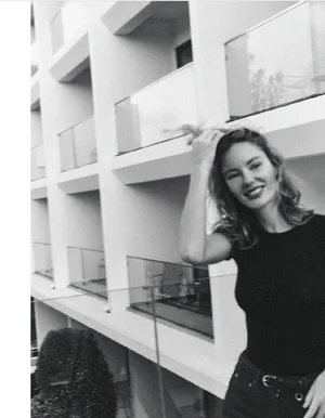 Black and white portrait of a smiling female model standing on a balcony against a modern multi-story architectural building exterior.